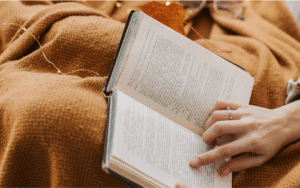 Woman reads book with blanket on her lap.